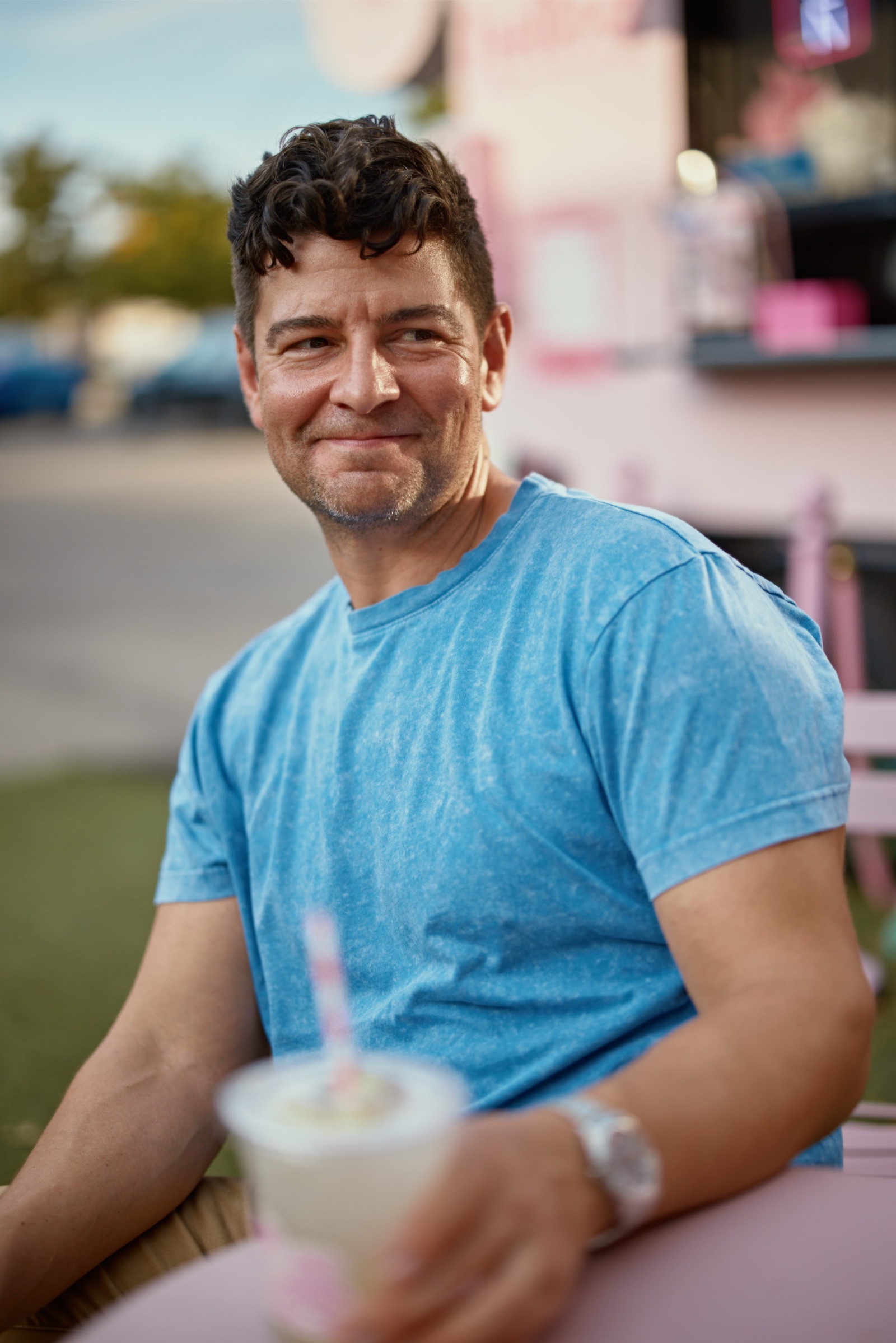 Relaxed portrait of a man sitting outdoors with a drink during a dating profile photography session