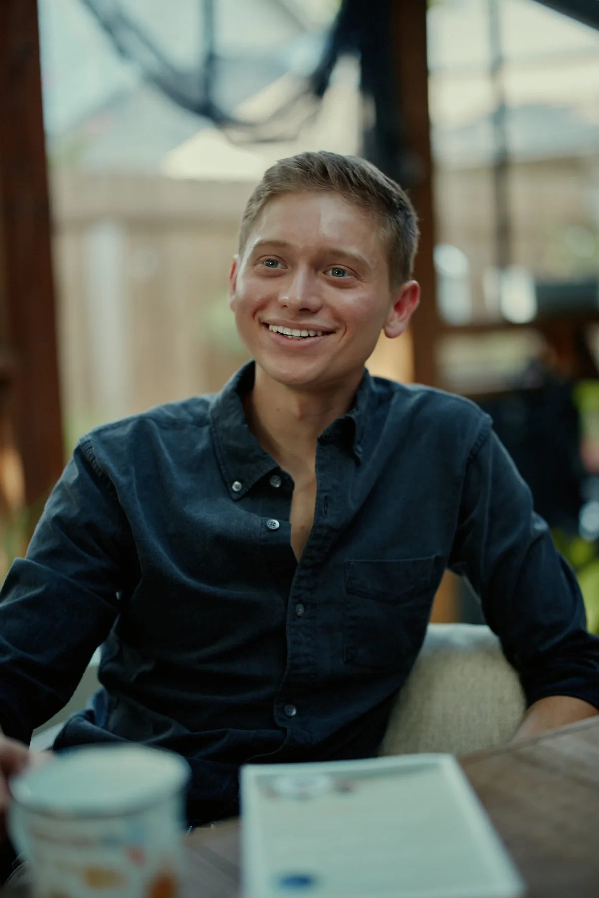 Smiling man in a dark shirt at an outdoor table, a relaxed portrait for a dating profile