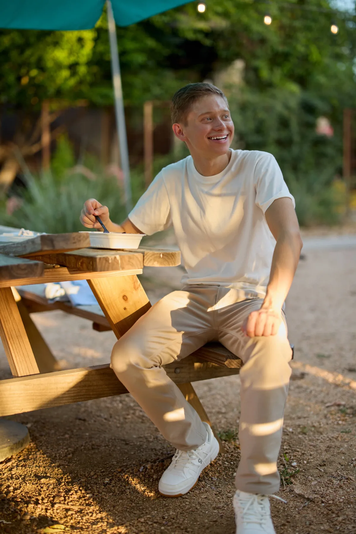 Laughing man in a white tee sitting on a picnic table at golden hour