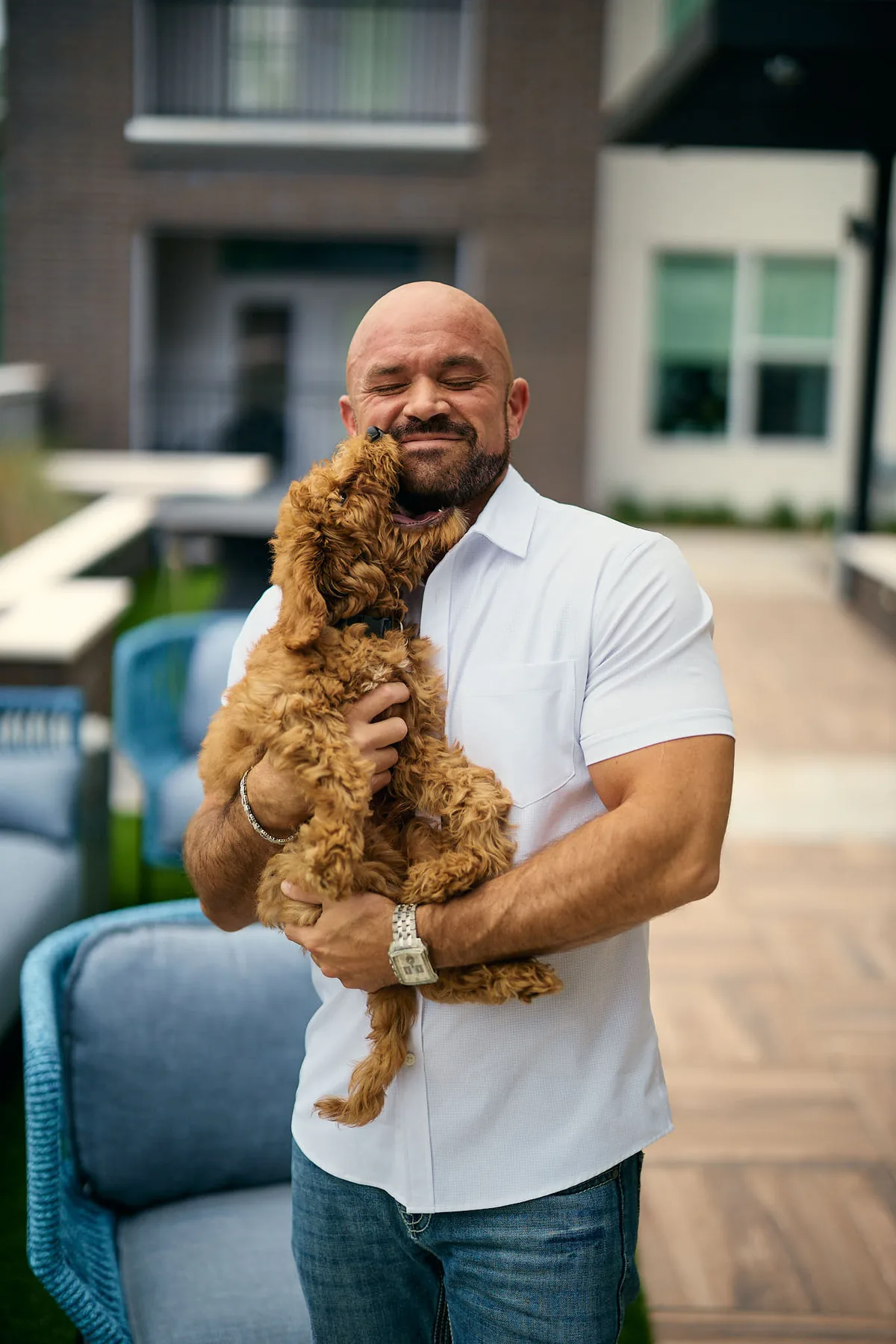Man in a white polo holding up a fluffy puppy on a patio, a classic puppy shot for a dating profile