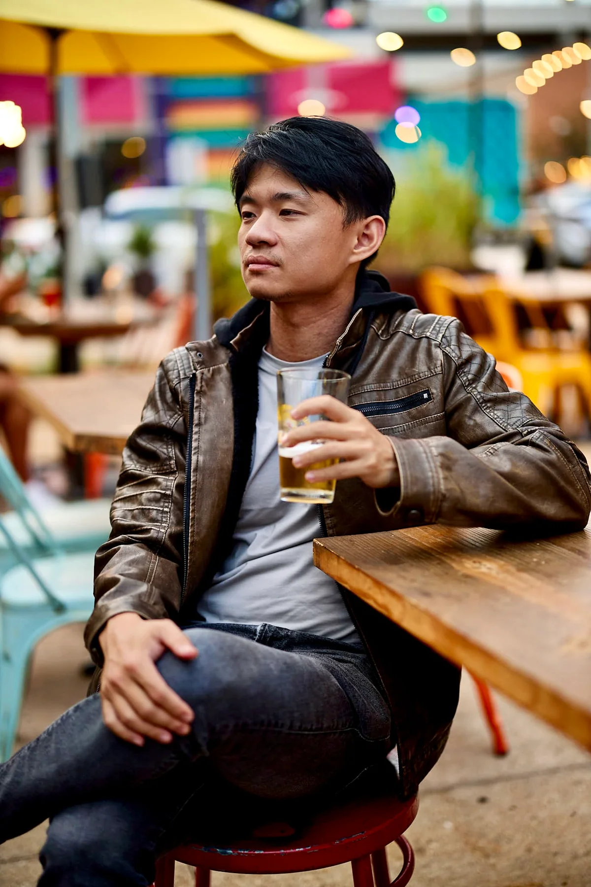 Man in a brown leather jacket leaning on a bar table with a beer, a style shot for a dating profile