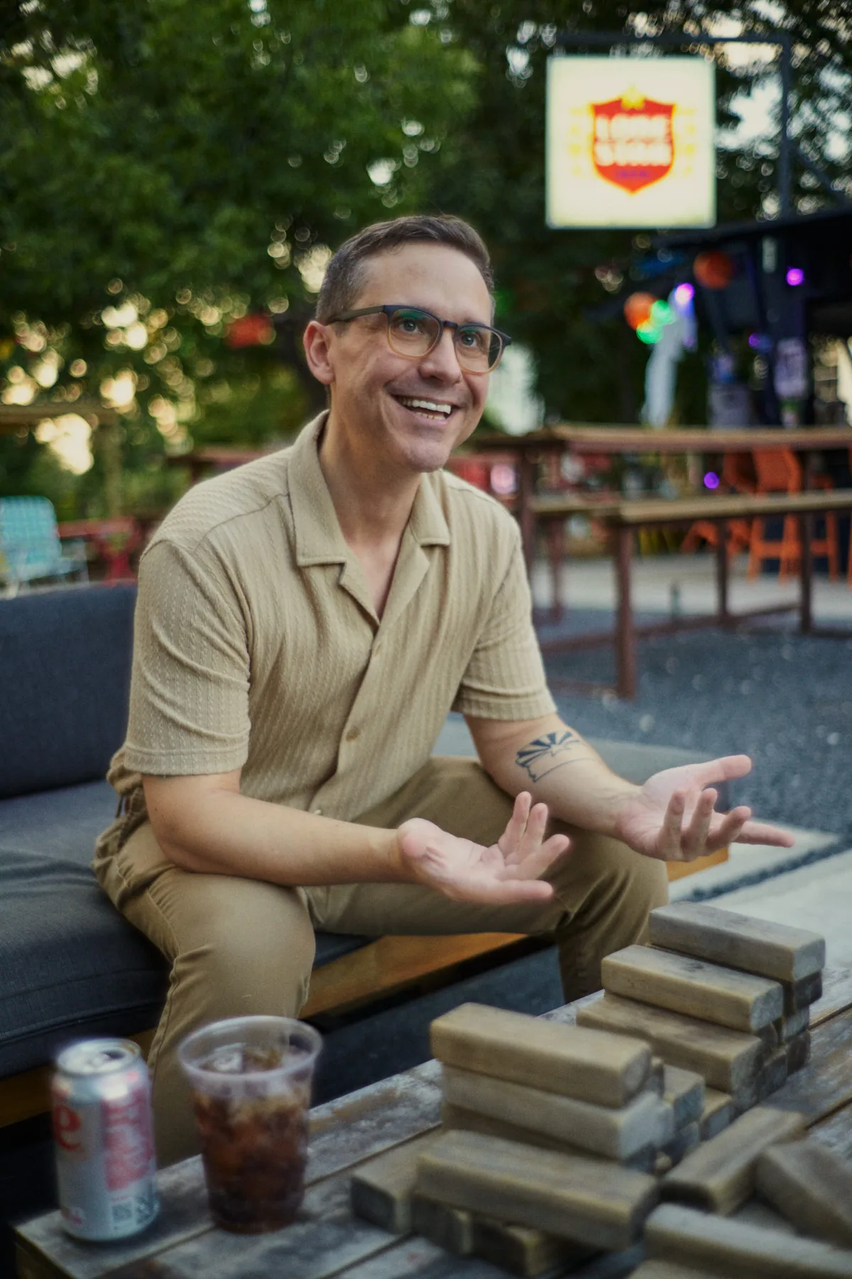 Man laughing on a patio couch with a drink, a candid reaction shot for a dating profile