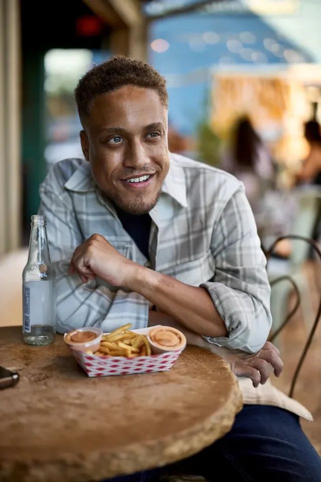 Man relaxing at an outdoor food hall with french fries, a casual Austin dating profile photo