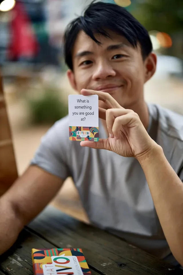Man smiling with a party card game at an outdoor table, a fun personality shot from an Austin dating photography session