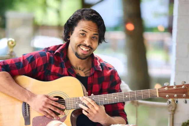 Inviting portrait of a Black man holding a guitar and smiling at the camera for his dating profile