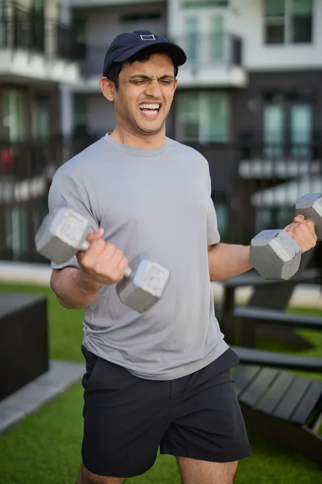 Young man in athletic clothing lifting dumbbells outdoors in front of a modern Austin apartment building
