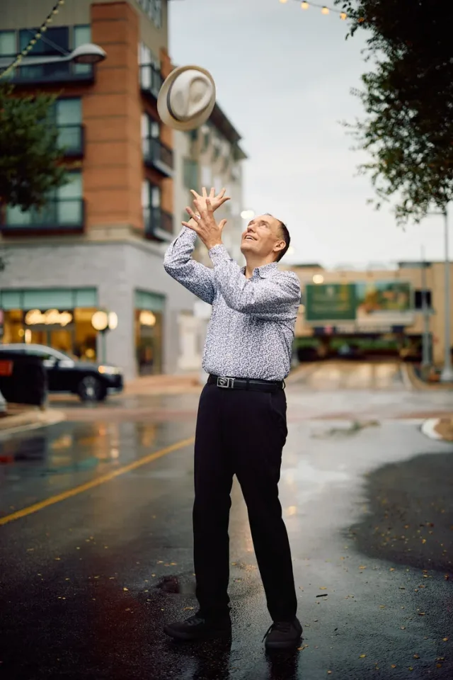 Man tossing a hat in the air on a city street, a playful outdoor shot from an Austin dating profile photography session