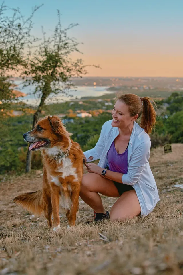 Woman with her dog and Lady Bird Lake behind her at sunset, a fun Austin dating profile photo