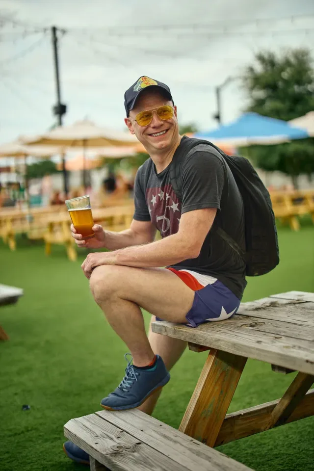 Man holding a pint at a colorful outdoor beer garden, a lifestyle shot from an Austin dating photography session