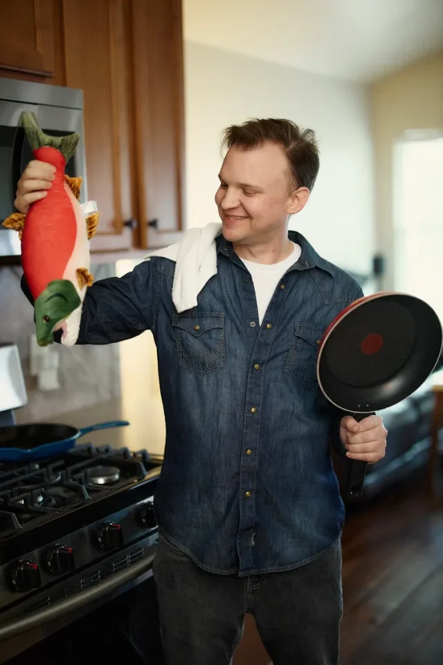 Man holding a plush toy fish in a kitchen as a joke for his dating profile