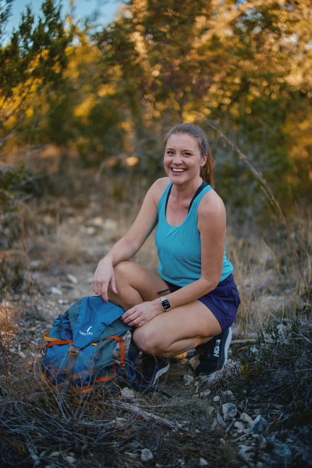 Smiling woman crouching on a hiking trail with her backpack, a dating profile photo by Eli Samuel