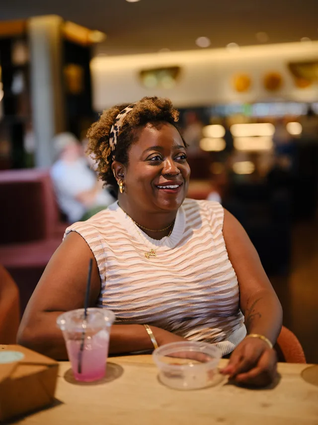 Smiling woman with a pink drink at a restaurant table, a dating profile photo by Eli Samuel